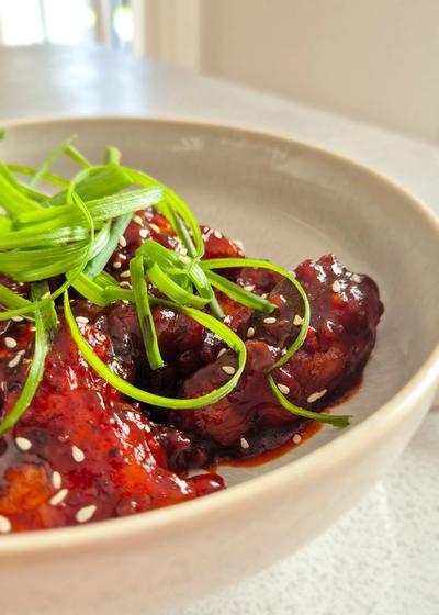 Koreanisches Fried Chicken - Yangnyeom - mit Frühlingszwiebeln und Sesam in einer Schale serviert.