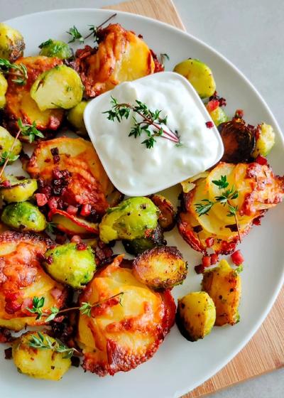 Knusprige Kartoffeltürmchen mit Käse und Butter, serviert mit gebratenem Rosenkohl und Speck auf einem Teller – golden, würzig und perfekt für den Herbst.