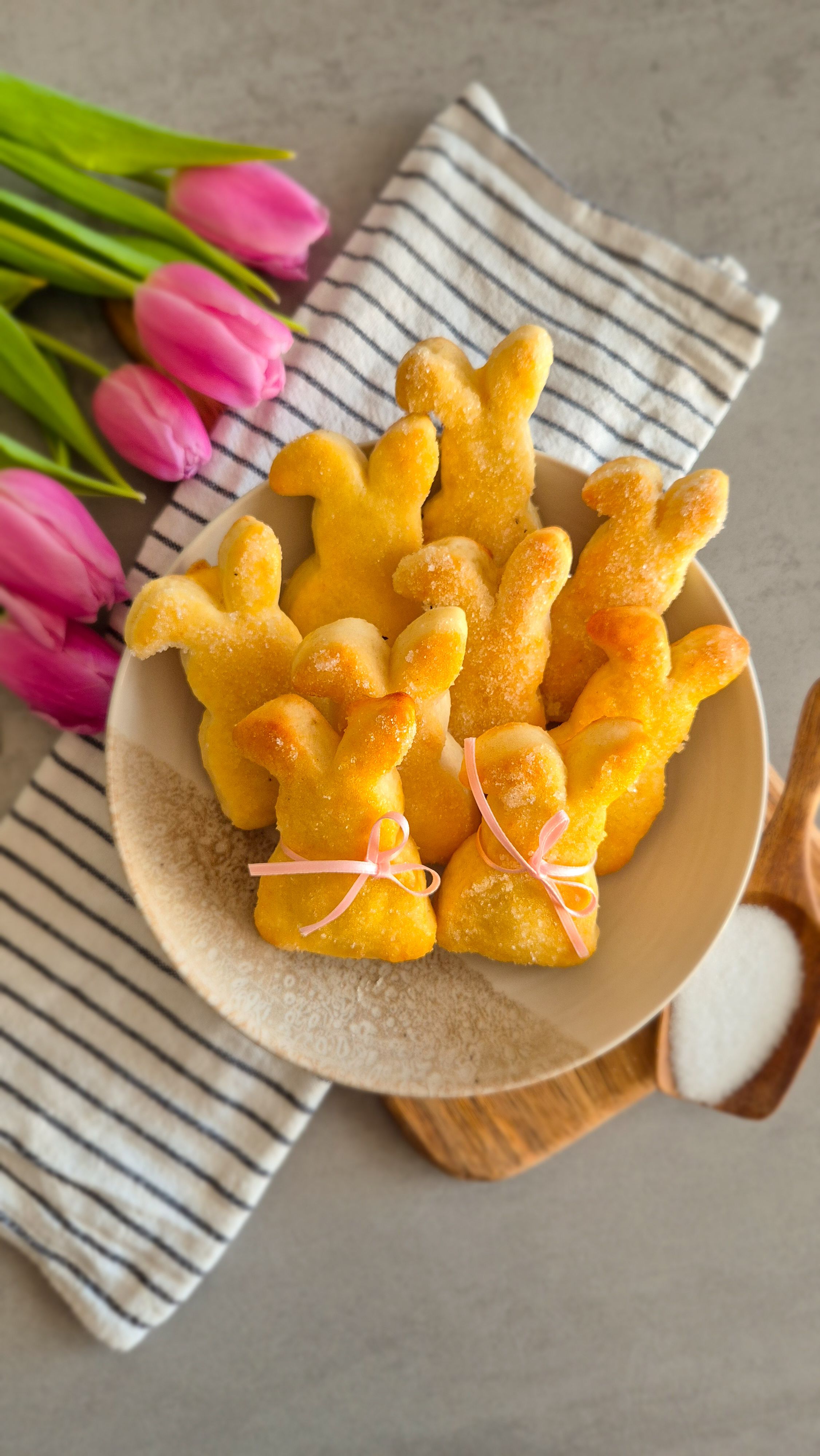 Ein paar Quarkhasen aus Quark-Öl-Teig auf einem rustikalen Teller neben pinken Tulpen zu Ostern.