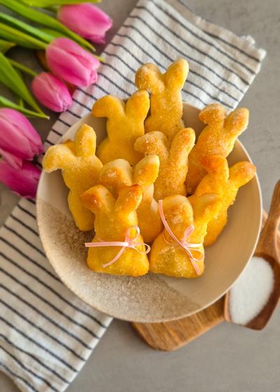 Ein paar Quarkhasen aus Quark-Öl-Teig auf einem rustikalen Teller neben pinken Tulpen zu Ostern.