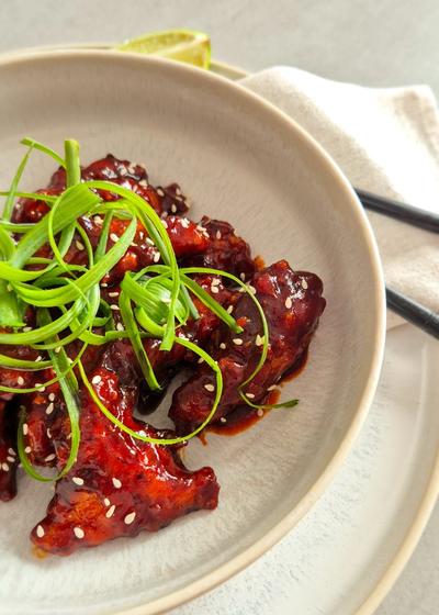 Koreanisches Fried Chicken - Yangnyeom - mit Frühlingszwiebeln und Sesam in einer Schale serviert.