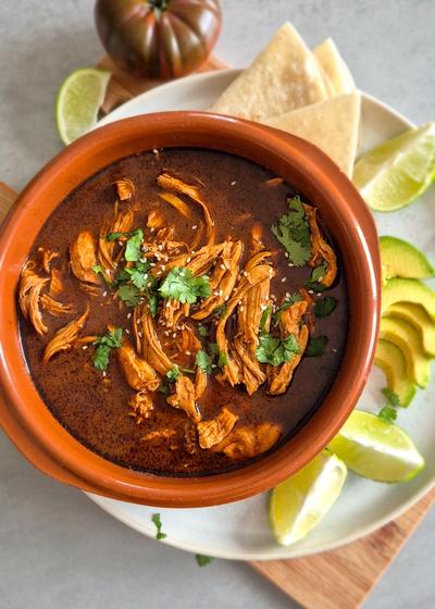 Authentisches Mole Poblano in einer Cazuela mit Avocado und Tortilla.
