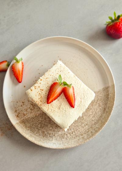 Ein Stück Tres Leches Cake mit Erdbeeren auf einem rustikalen Teller serviert.