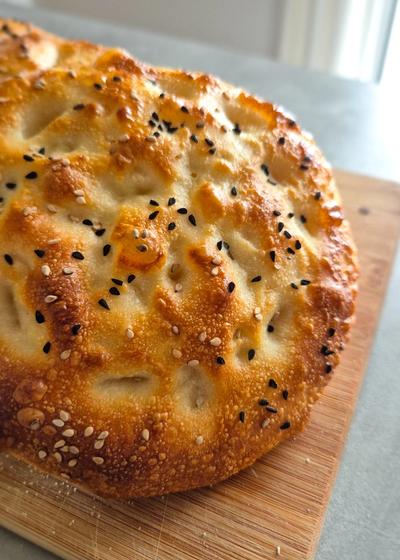 Selbstgemachtes türkisches Fladenbrot mit Sesam und Schwarzkümmel auf einem Holzbrett in der Küche.