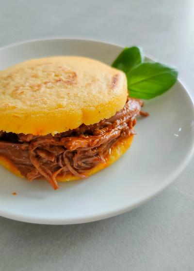 Venezolanische Arepas aus P.A.N. Maismehl mit Carne Mechada auf einem Teller.