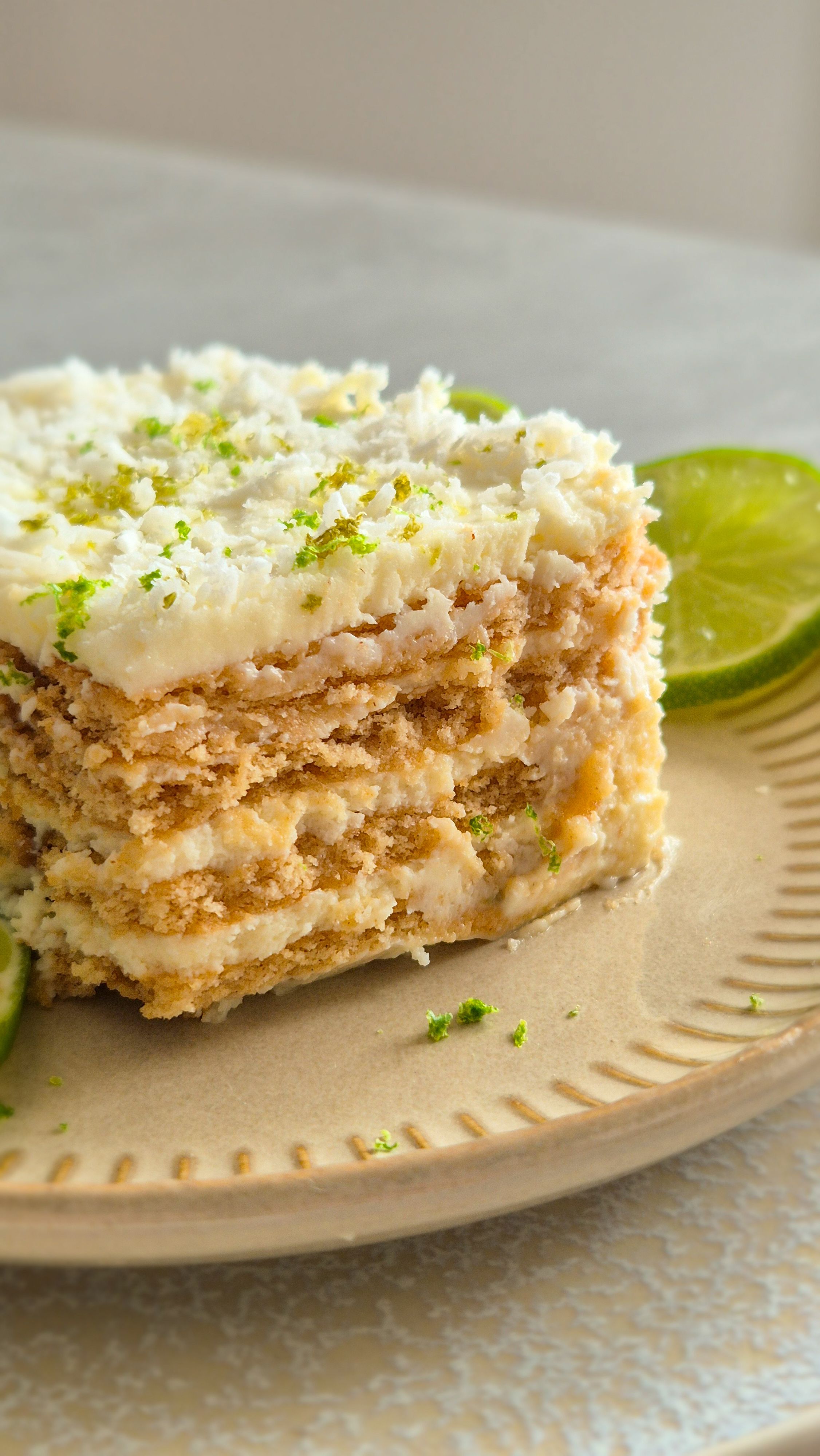 Ein Stück Carlota de Limón (mexikanischer Limettenkuchen) auf einem beigen Teller mit Limettenscheiben serviert. 