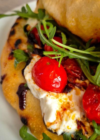 Ein Pizzasandwich mit Pesto Rosso, Burrata und Rucola auf einem Teller.