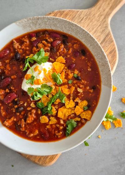 Würziges Chili Con Carne mit Crema und Nachos in einem tiefen Teller serviert.