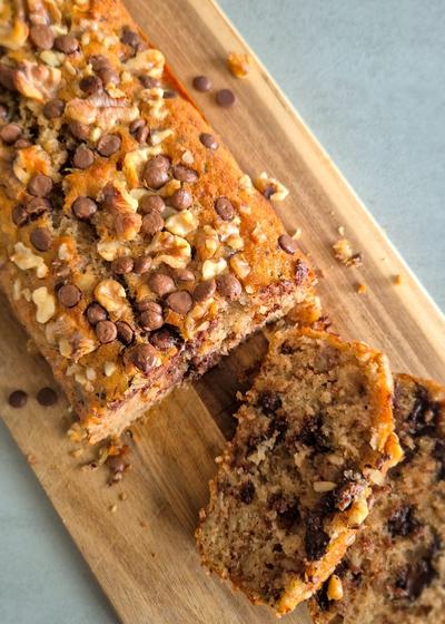 Frisch gebackenes Chunky Monkey Bananenbrot mit Walnüssen und Schokoladen-Chunks auf einem Holzbrett.