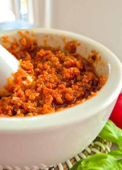 Rotes Pesto - Pesto Rosso - aus getrockneten Tomaten, Mandeln und Pinienkernen in einem Mörser.