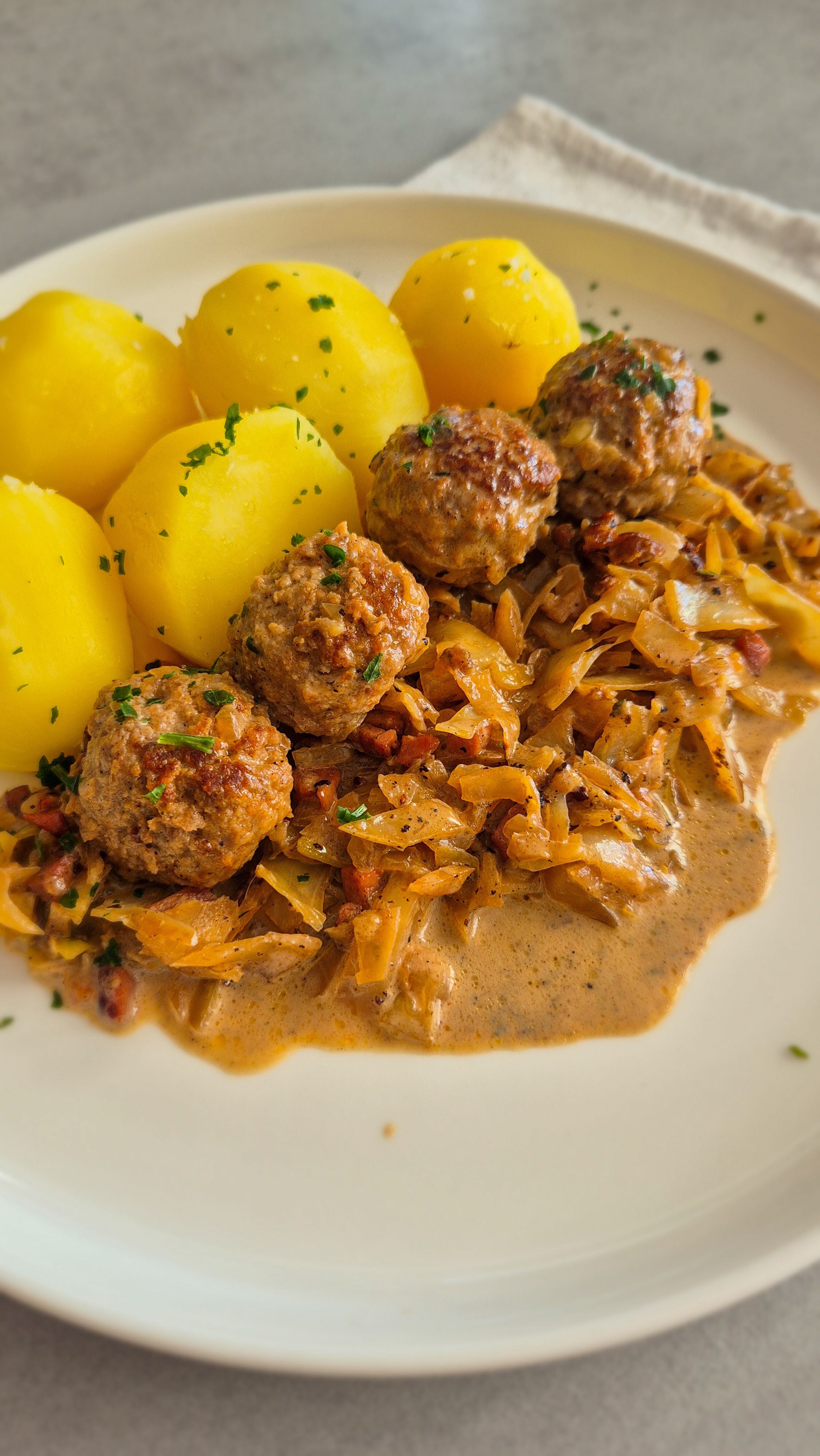 Hackbällchen mit gedünstetem Weißkohl in cremiger Sauce und Salzkartoffeln auf einem Teller.