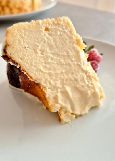 Ein Stück cremiger San Sebastian Cheesecake mit einer dunkelbraun karamellisierten Kruste auf einem Teller neben frischen Erdbeeren.