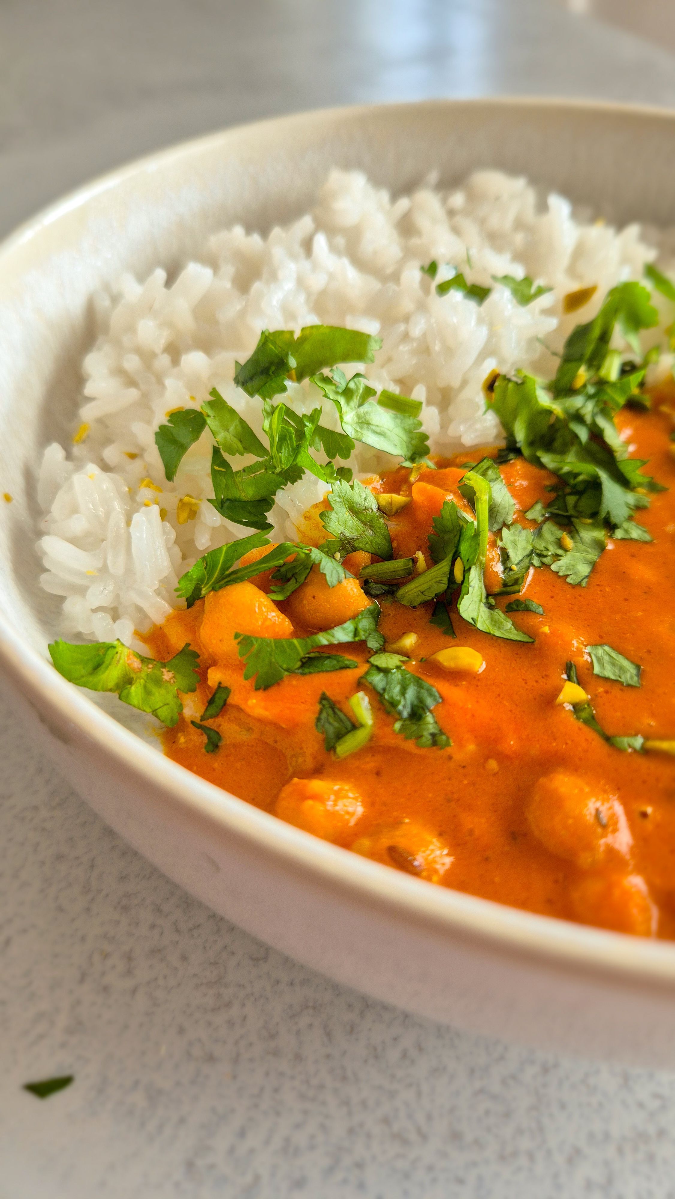 hausgemachtes, würziges Curry mit Kichererbsen und Hähnchenfleisch nach nordindischer Art in einer Schale mit Koriander serviert.