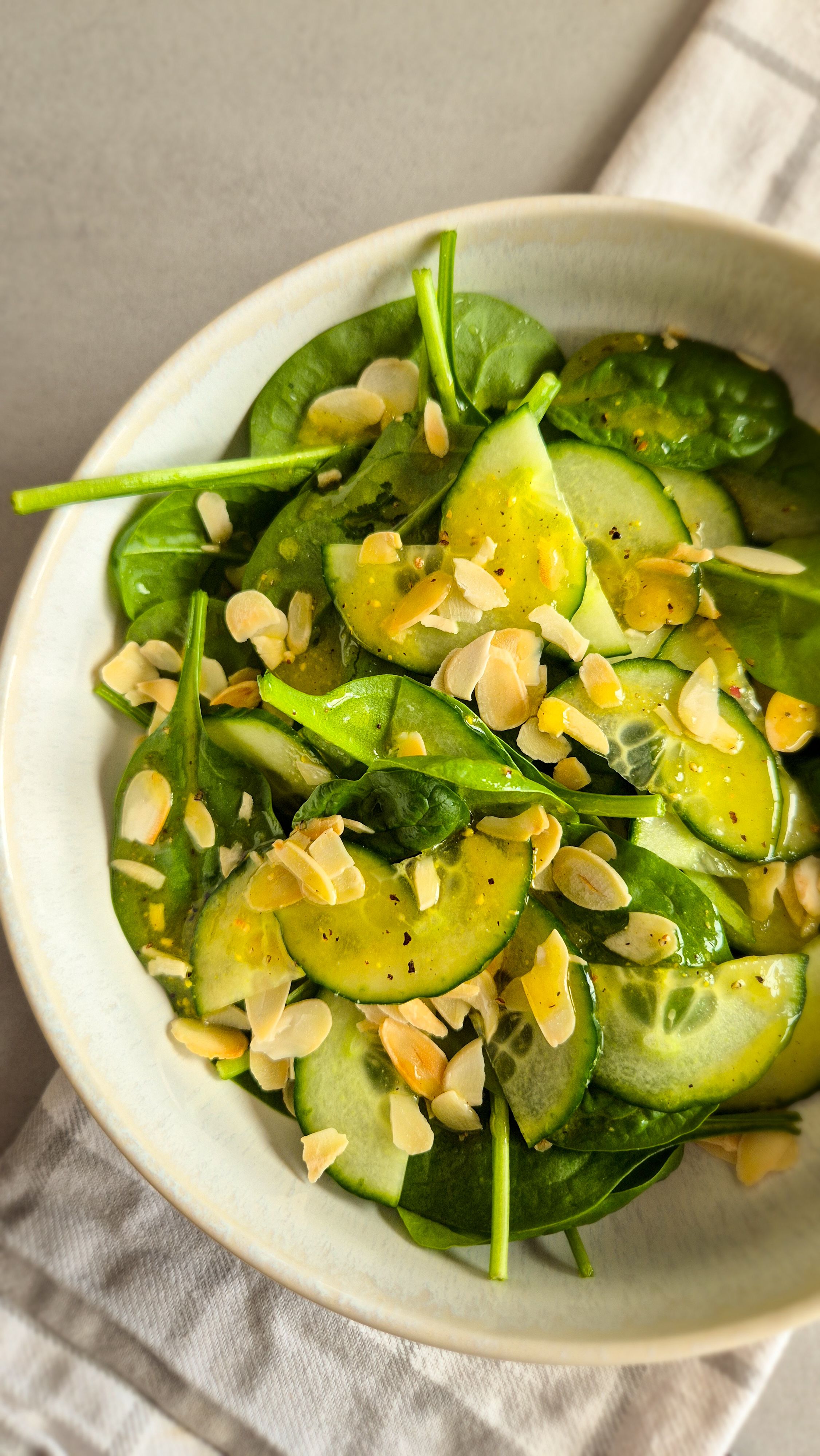 Ein erfrischender Blattsalat mir Gurken und Dressing in einer Schale mit Mandeln.