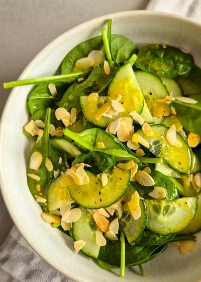Ein erfrischender Blattsalat mir Gurken und Dressing in einer Schale mit Mandeln.