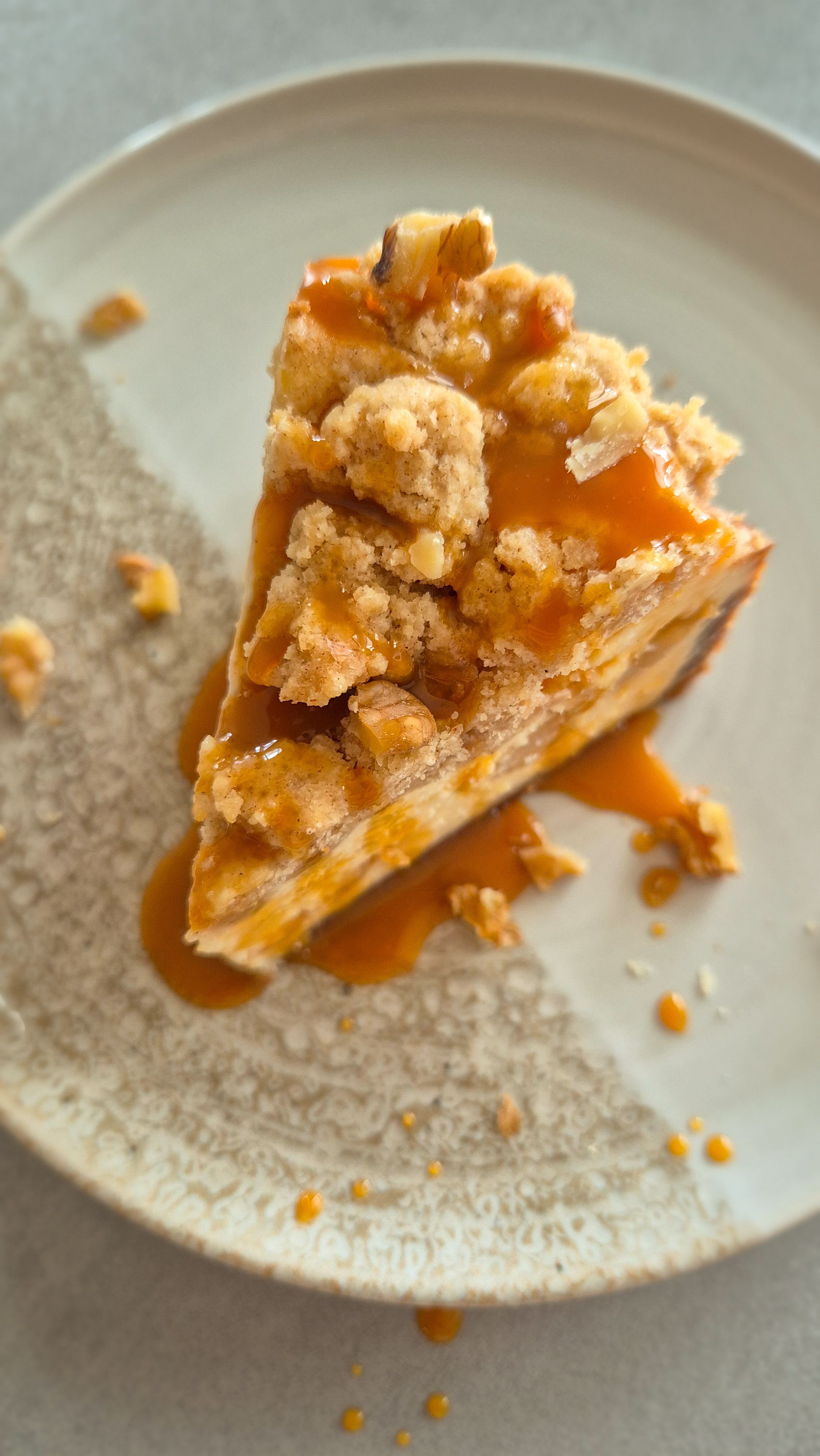 Ein Stück cremiger Cheesecake mit fruchtig, weicher Apfel-Zimt-Schicht und Knusper-Streuseln auf einem Teller serviert.