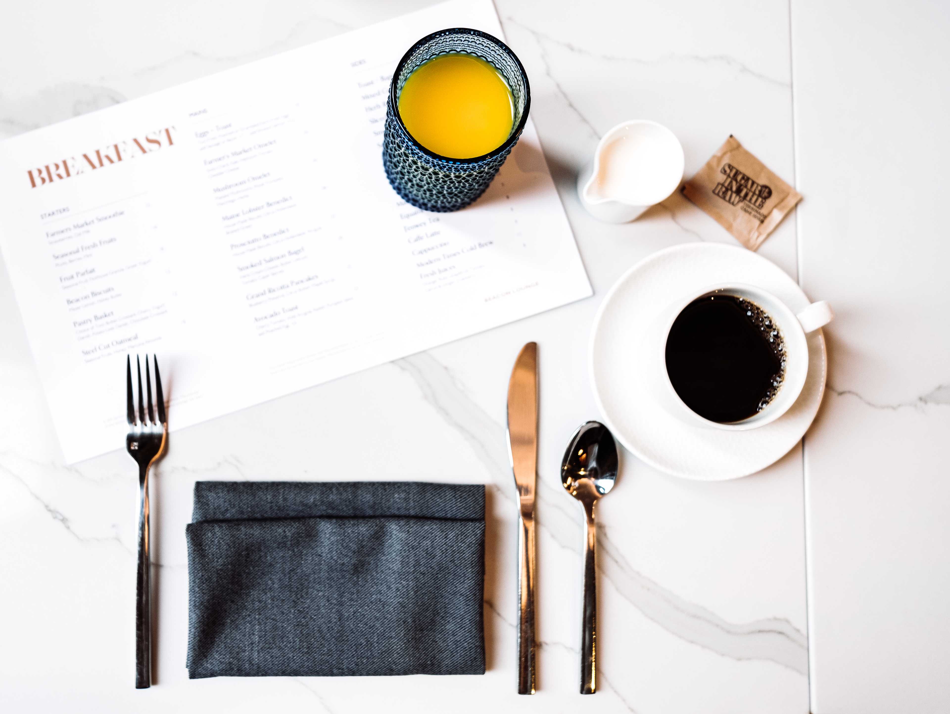 a breakfast menu with orange juice and forks on a marble table.