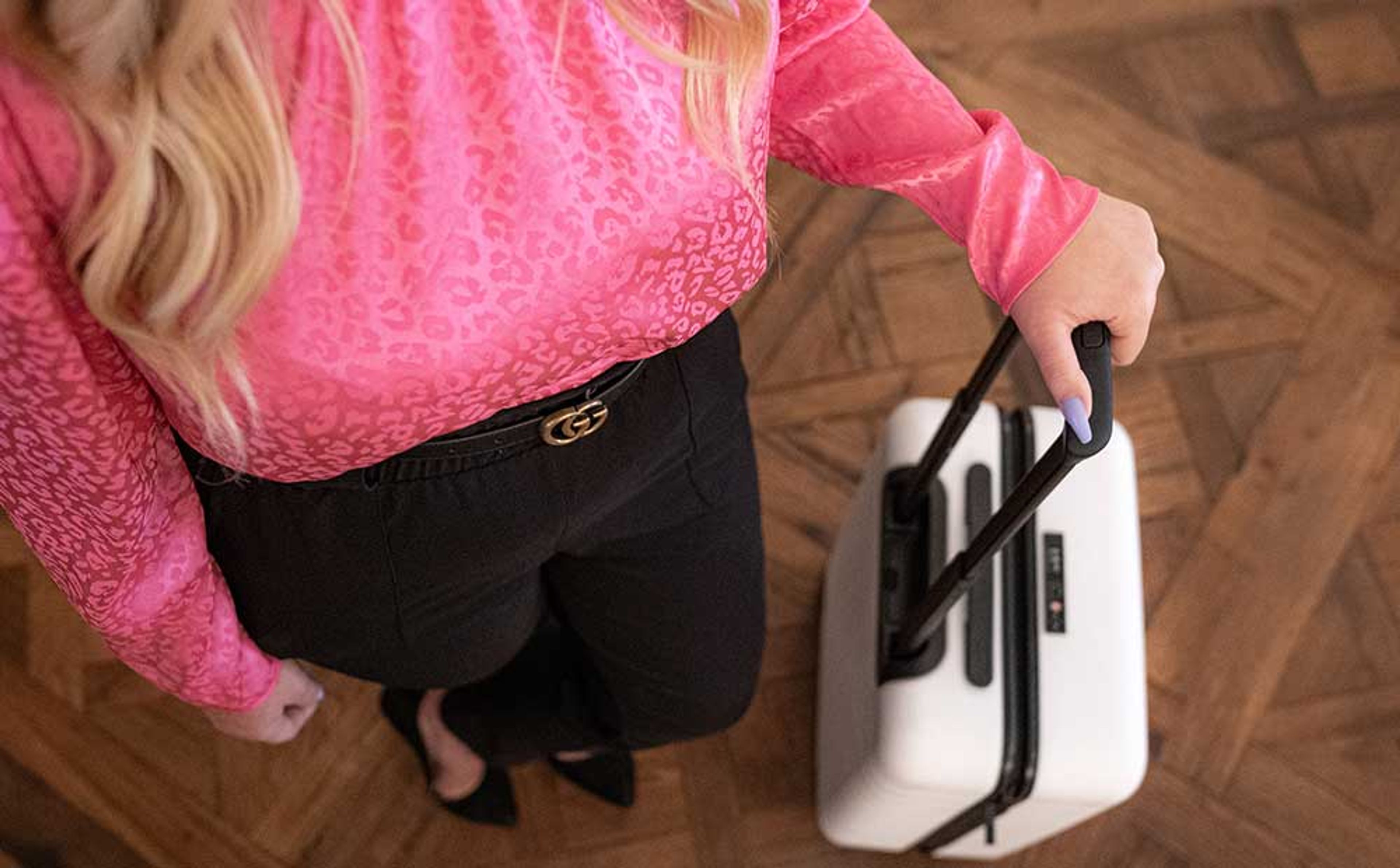 woman in a pink blouse rolling a white suitcase