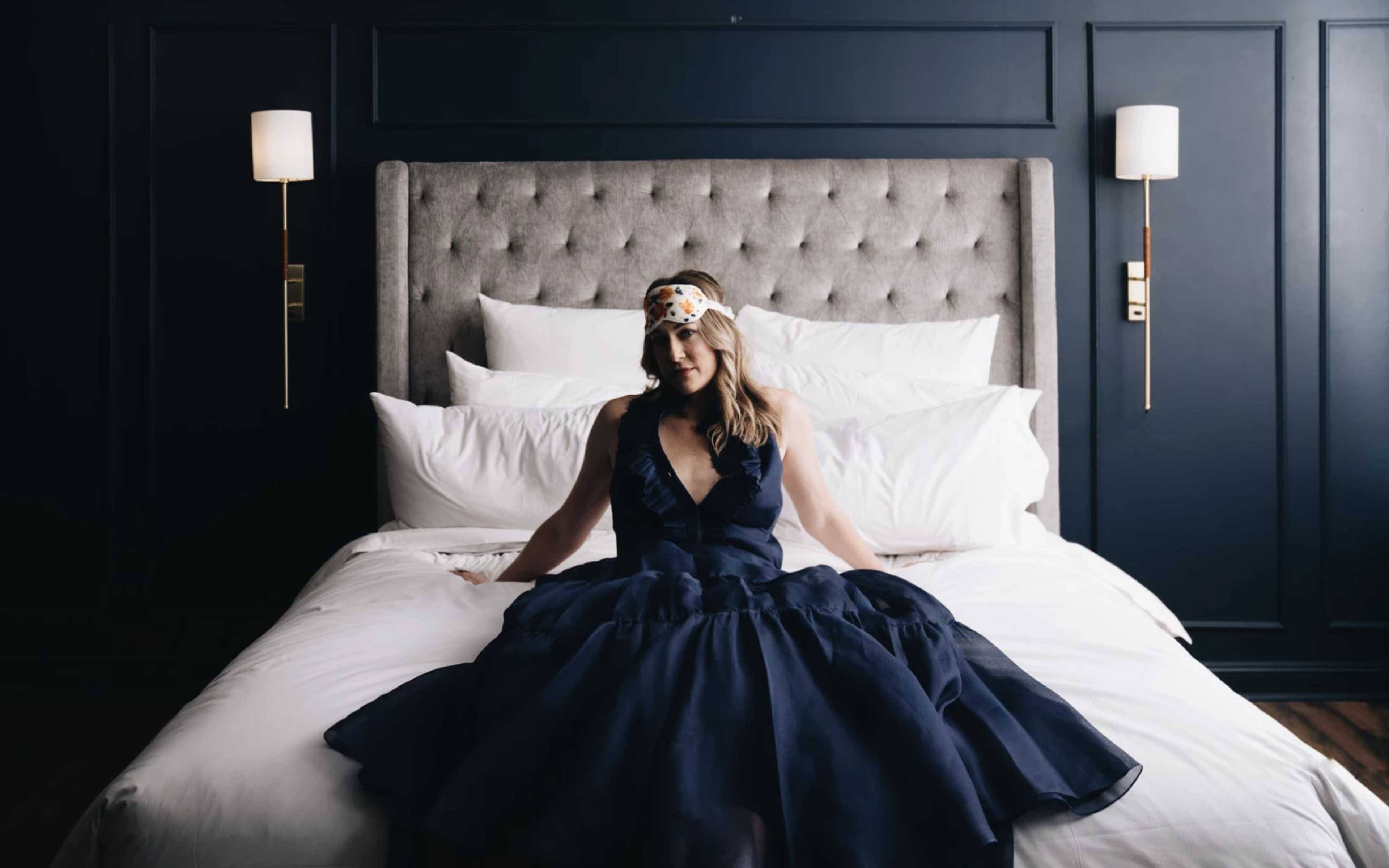 a woman in a blue dress sitting on a bed.