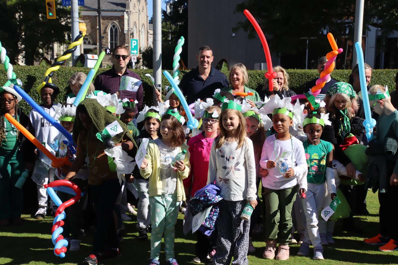 Foule d’enfants avec des couronnes vertes, des épées en ballons et des drapeaux, devant les dignitaires