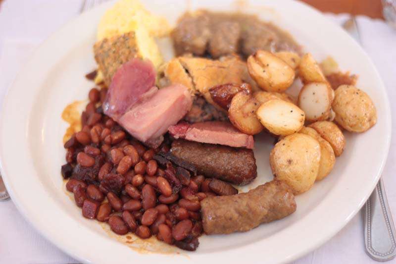 Un déjeuner aux oeufs brouillés, jambon, saucisses, fèves au lard et petites patates au four