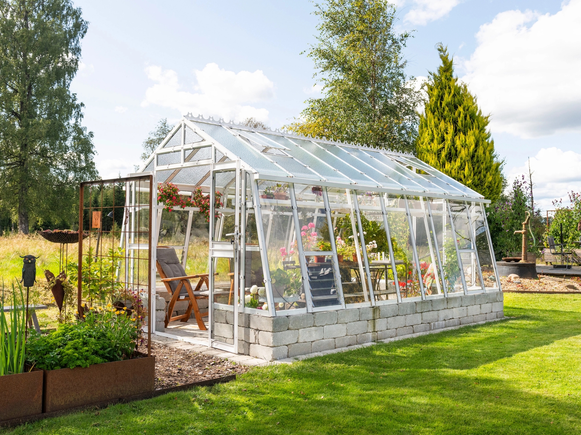 Växthus Primus 303 i en trädgård med inredning i växthuset