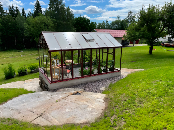 Växthus placerat i trädgård med odlingar