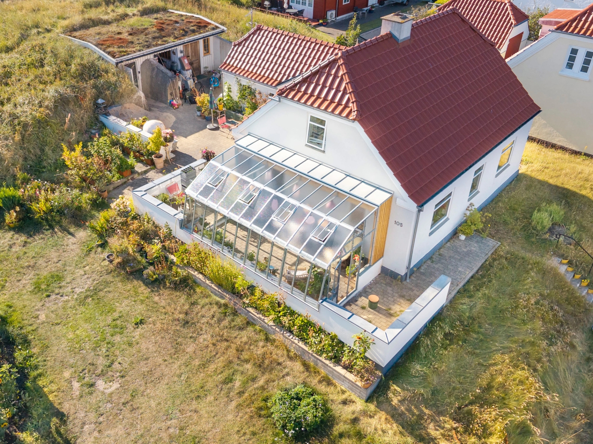 Drivhus Variant 275 mod væg monteret i en flot have i Danmark