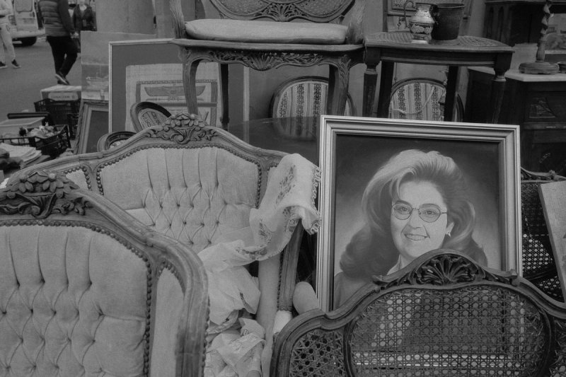 A framed studio portrait of a woman leaning against second-hand armchairs. Elaionas, photograph by Yannis Papanastasopoulos