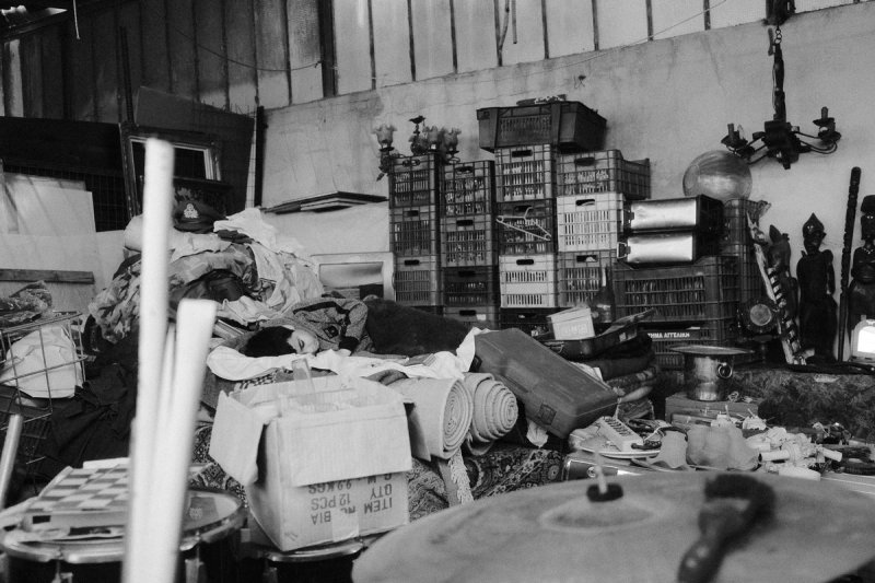 A dog asleep on a pile of goods inside a corrugated shed stacked with crates. Elaionas, photograph by Yannis Papanastasopoulos