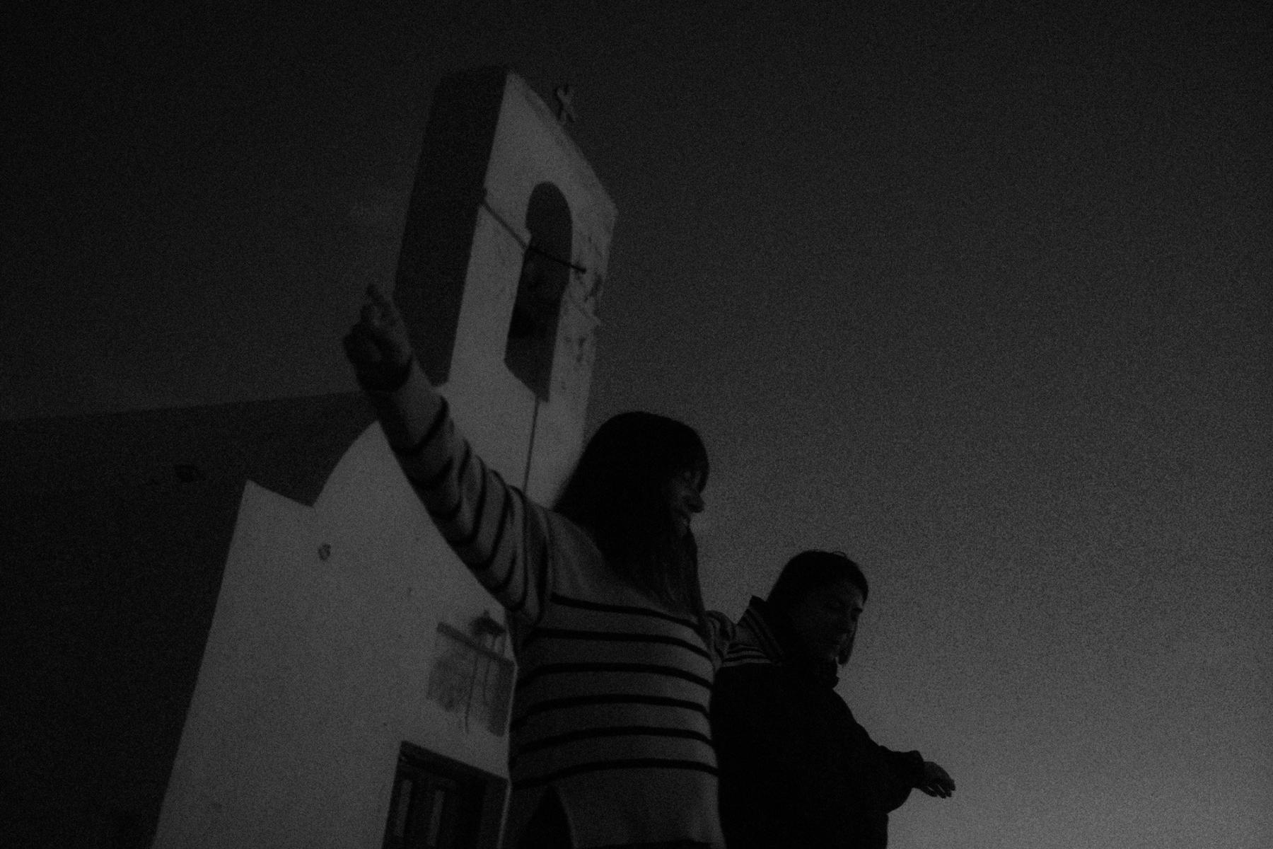 A woman reaching up beside a whitewashed bell tower at dusk