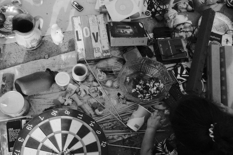 Junk laid out on the ground seen from above: a dartboard, a phone, a bunch of flowers. Elaionas, photograph by Yannis Papanastasopoulos