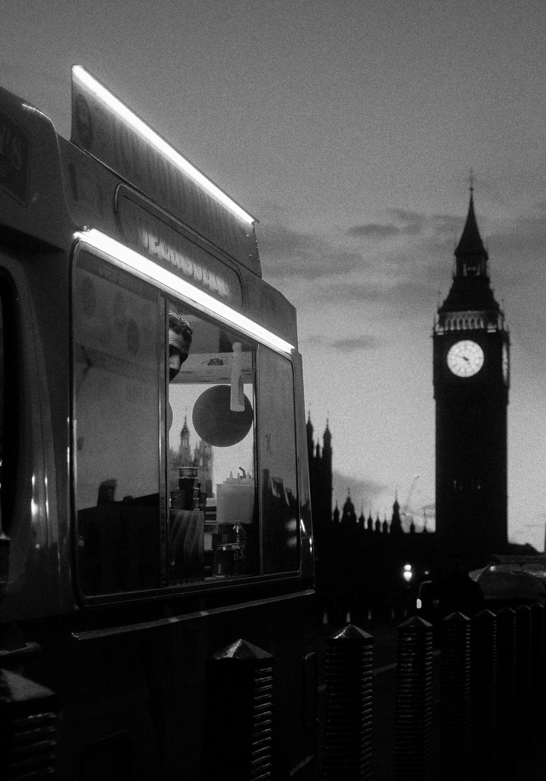 An ice cream van lit up at dusk with Big Ben and Parliament behind it