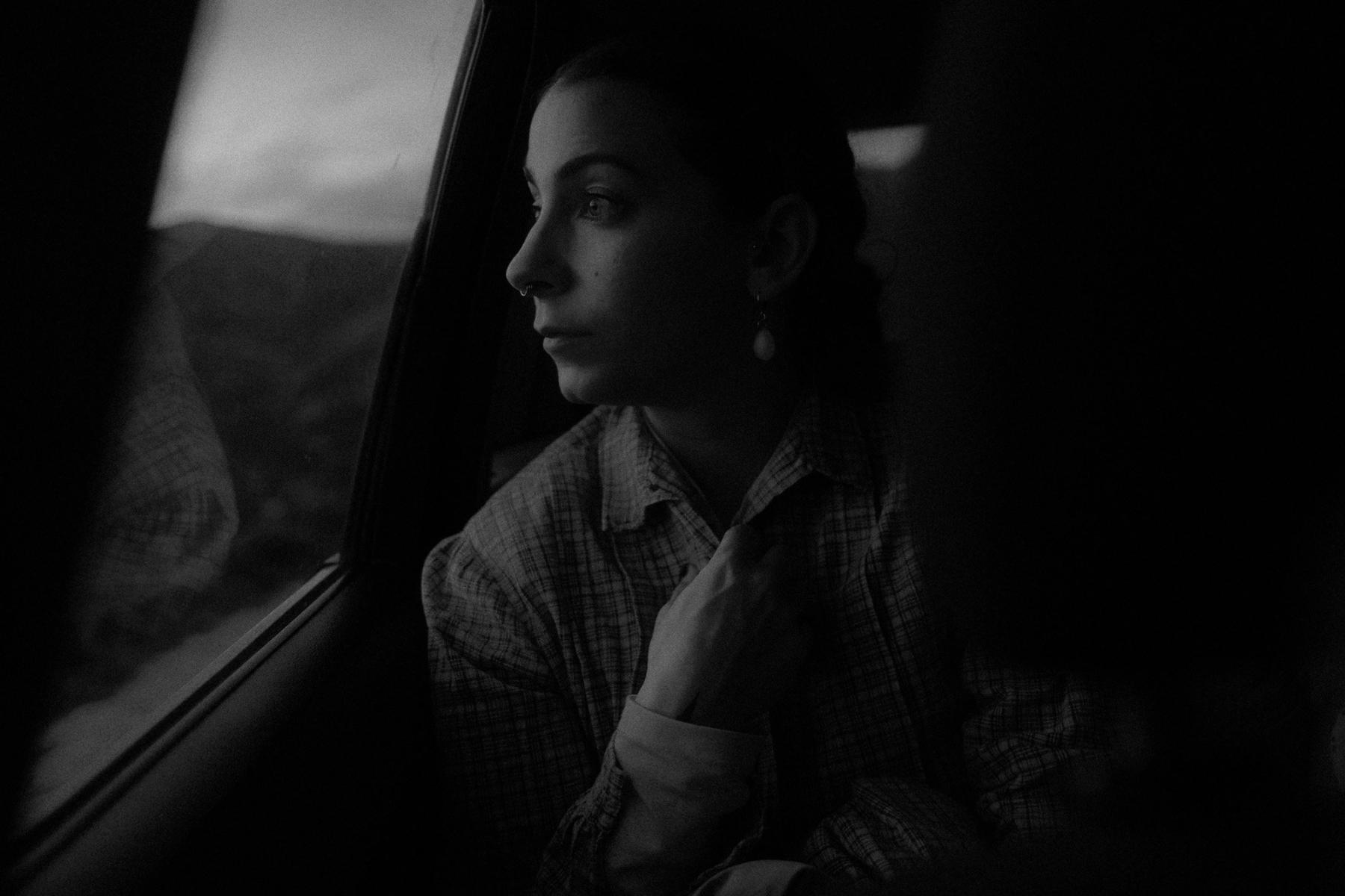 A woman looking out of a car window, hills passing behind the glass