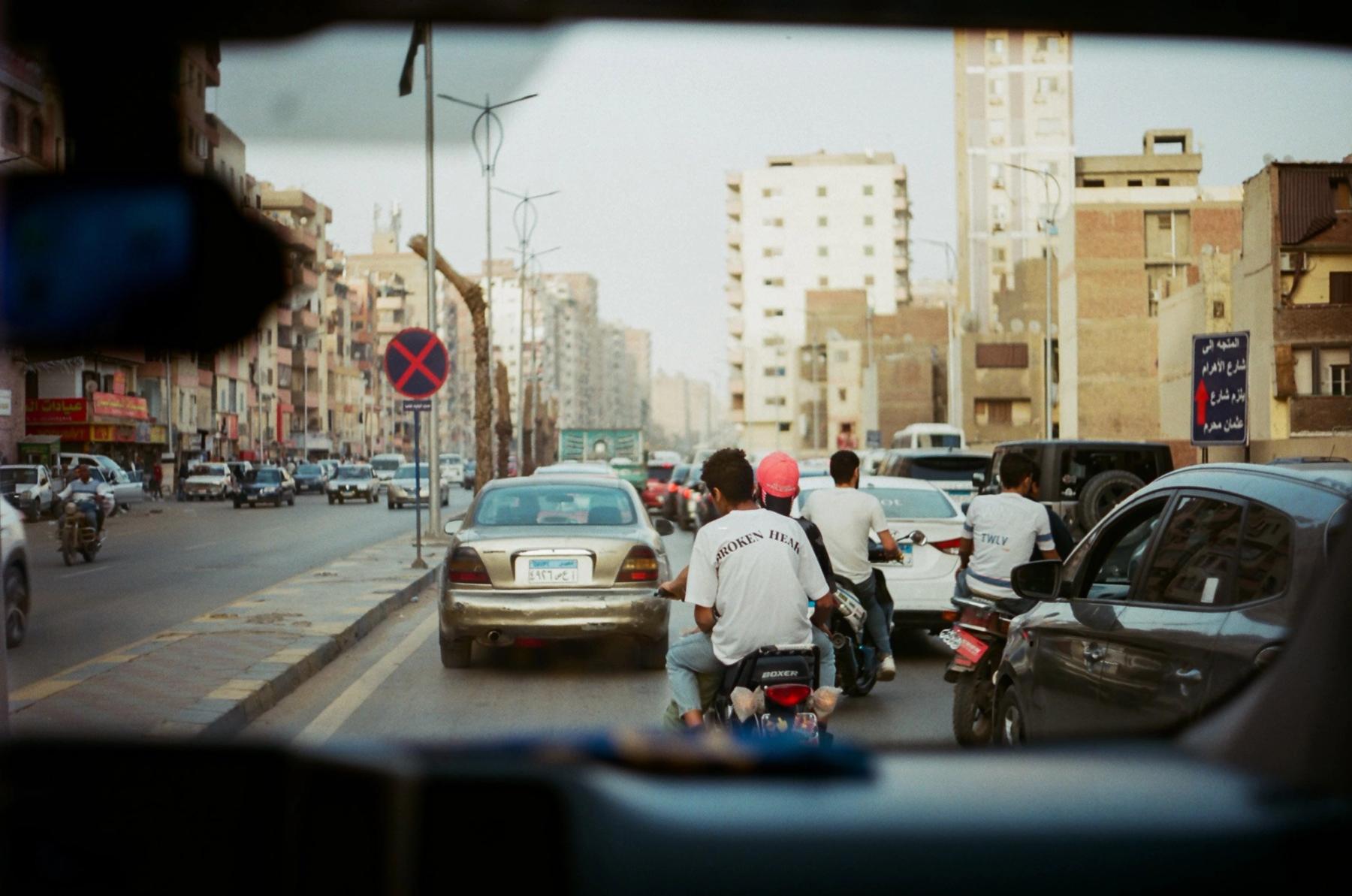 Traffic seen through a car windscreen, motorbikes threading between the cars