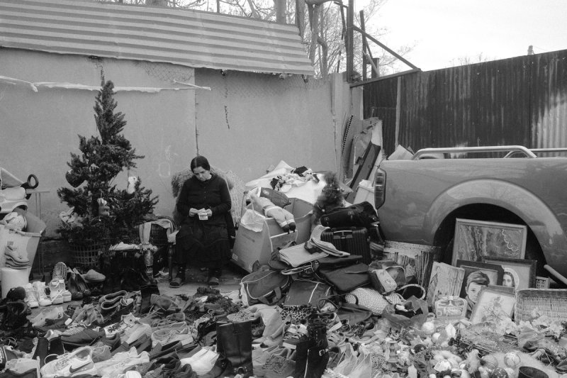 The same yard closer in, the woman reading something small in her hands amid the spread. Elaionas, photograph by Yannis Papanastasopoulos
