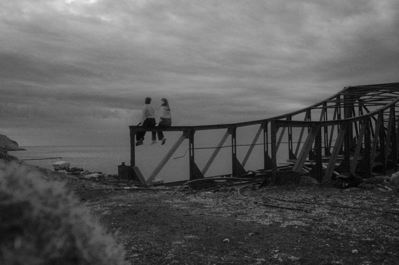 Two people sitting on the rusted iron loading pier, looking out to sea. Serifos, photograph by Yannis Papanastasopoulos