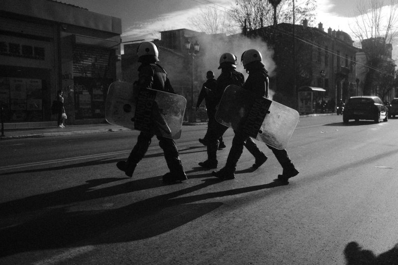 Four officers crossing the road with shields, long shadows ahead of them. Clashing Shadows, photograph by Yannis Papanastasopoulos