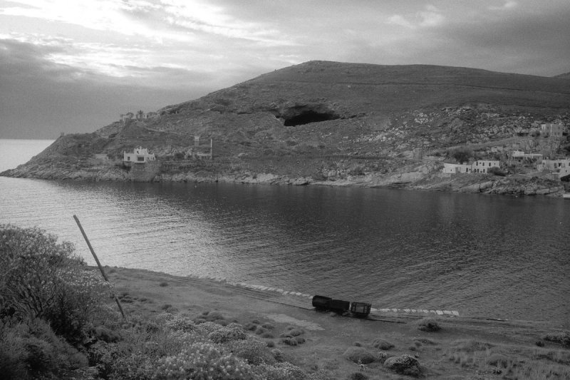 The bay at dusk, a cave mouth open in the headland above the water. Serifos, photograph by Yannis Papanastasopoulos