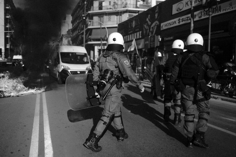 An officer walking toward black smoke rising from the street ahead. Clashing Shadows, photograph by Yannis Papanastasopoulos