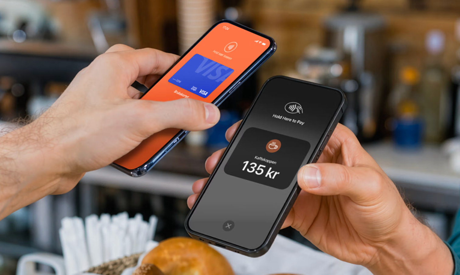Two hands hold smartphones for a mobile payment; one displays a Visa card, the other a 135 kr coffee purchase.