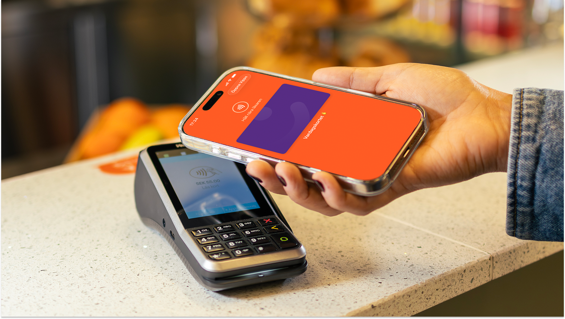 A hand holding a smartphone over a payment terminal for a contactless payment.