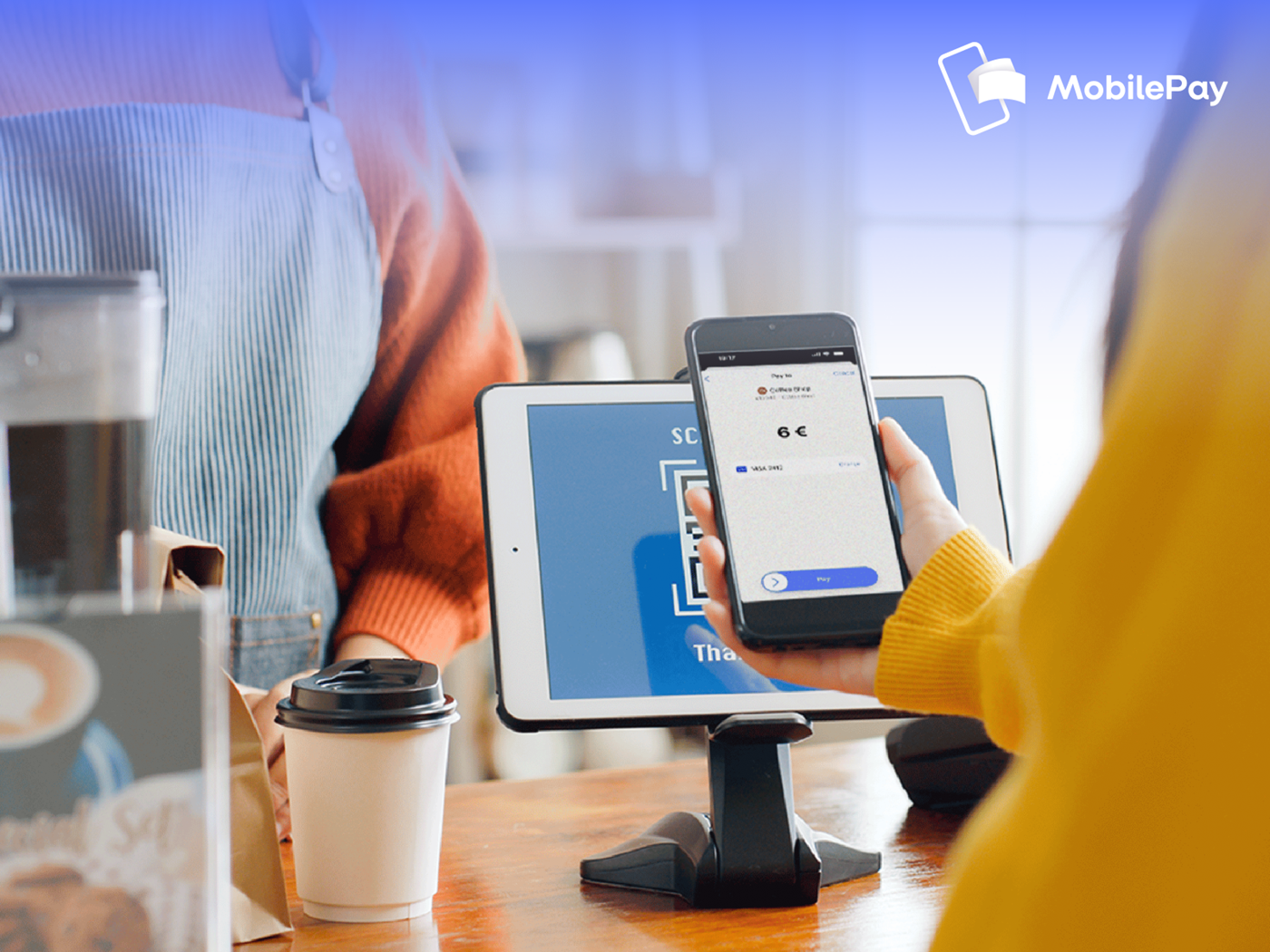 Customer scanning a QR code with a smartphone for mobile payment at a cafe counter.