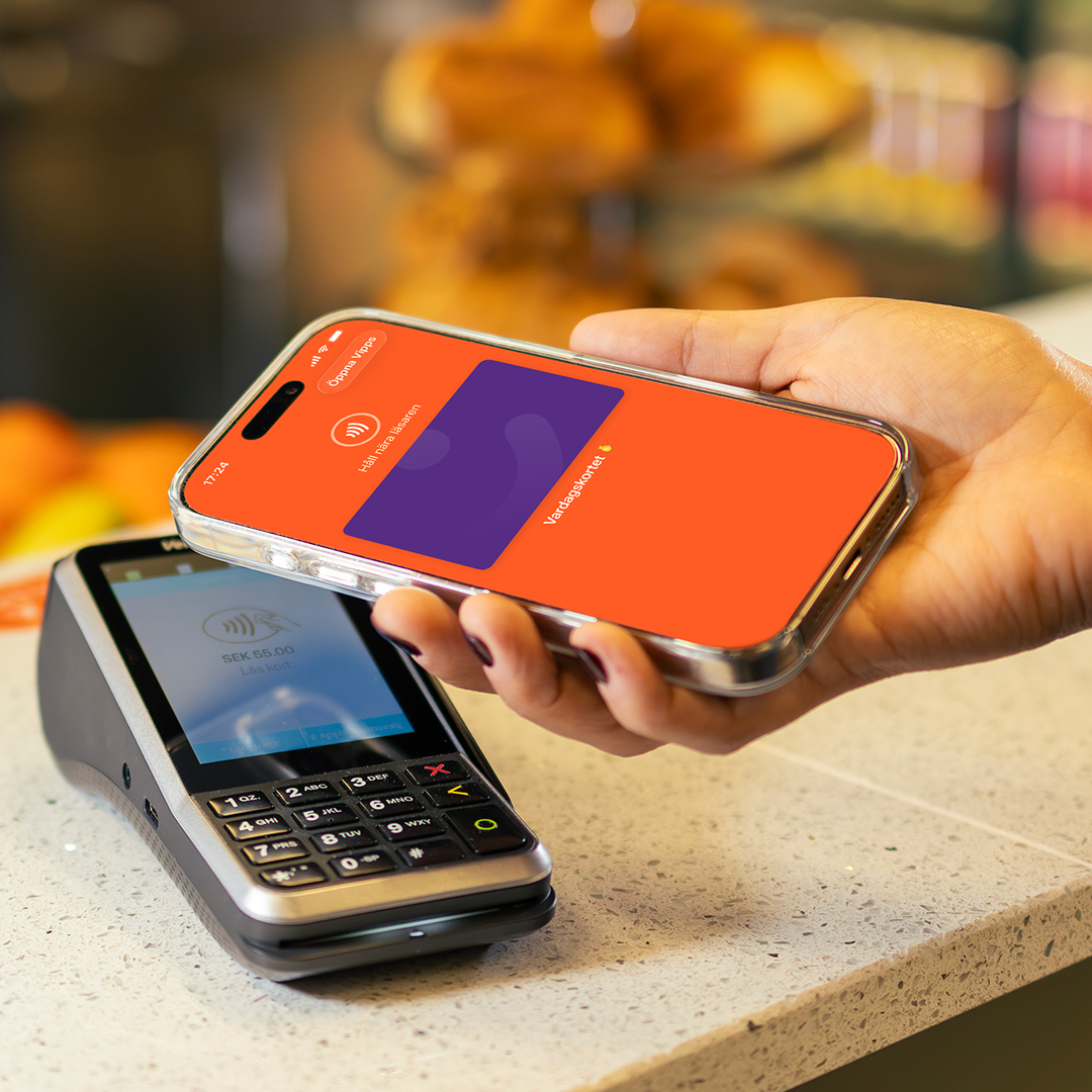 A hand holds a smartphone displaying a payment app over a payment terminal for a contactless transaction.