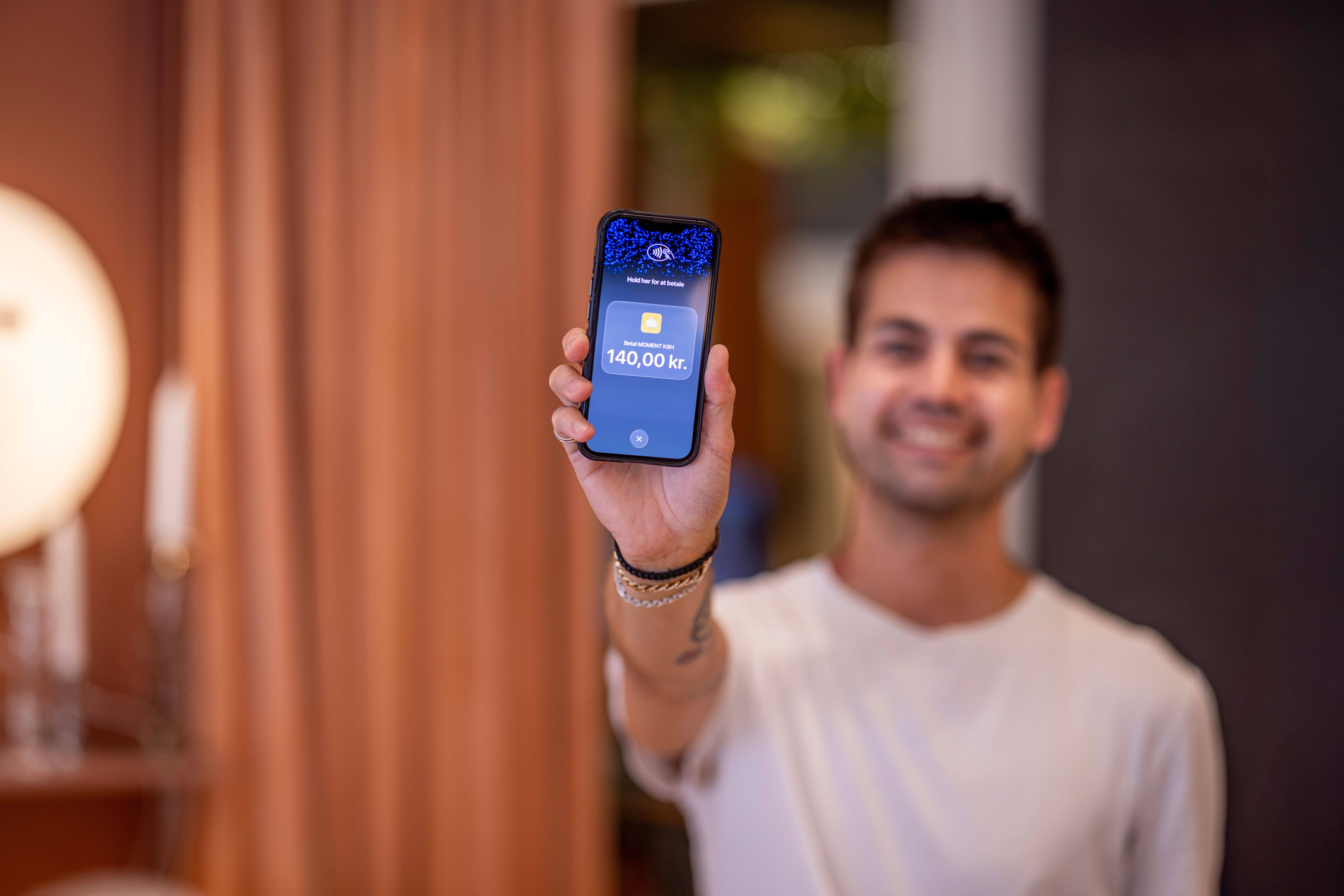 A man holds up a smartphone displaying 140,00 kr on its screen.