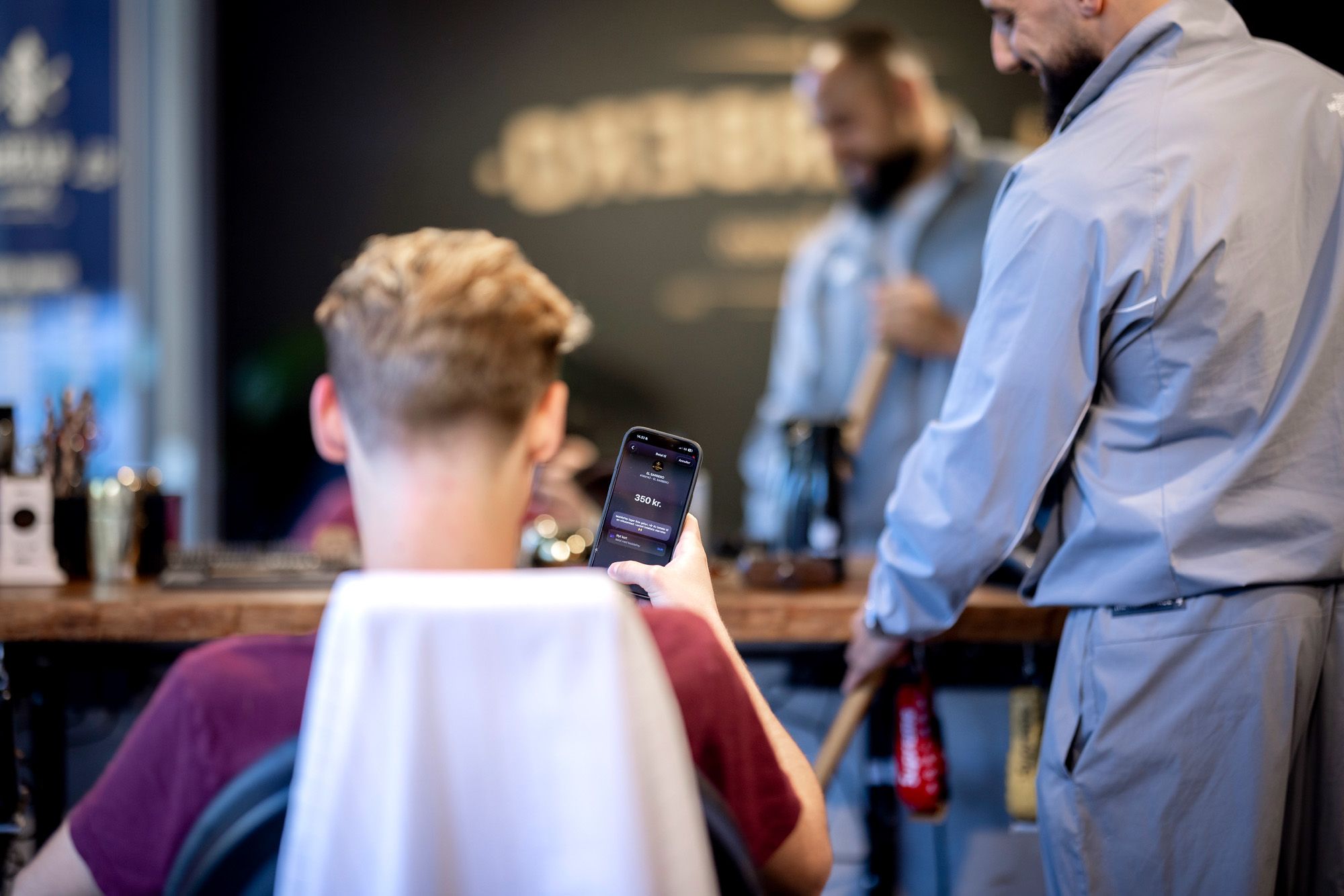 A customer in a barber shop looking at a payment app on their smartphone.