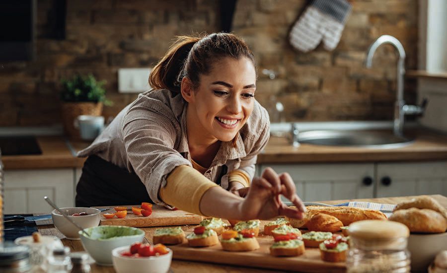 A smiling woman decorates small appetizers in a kitchen.