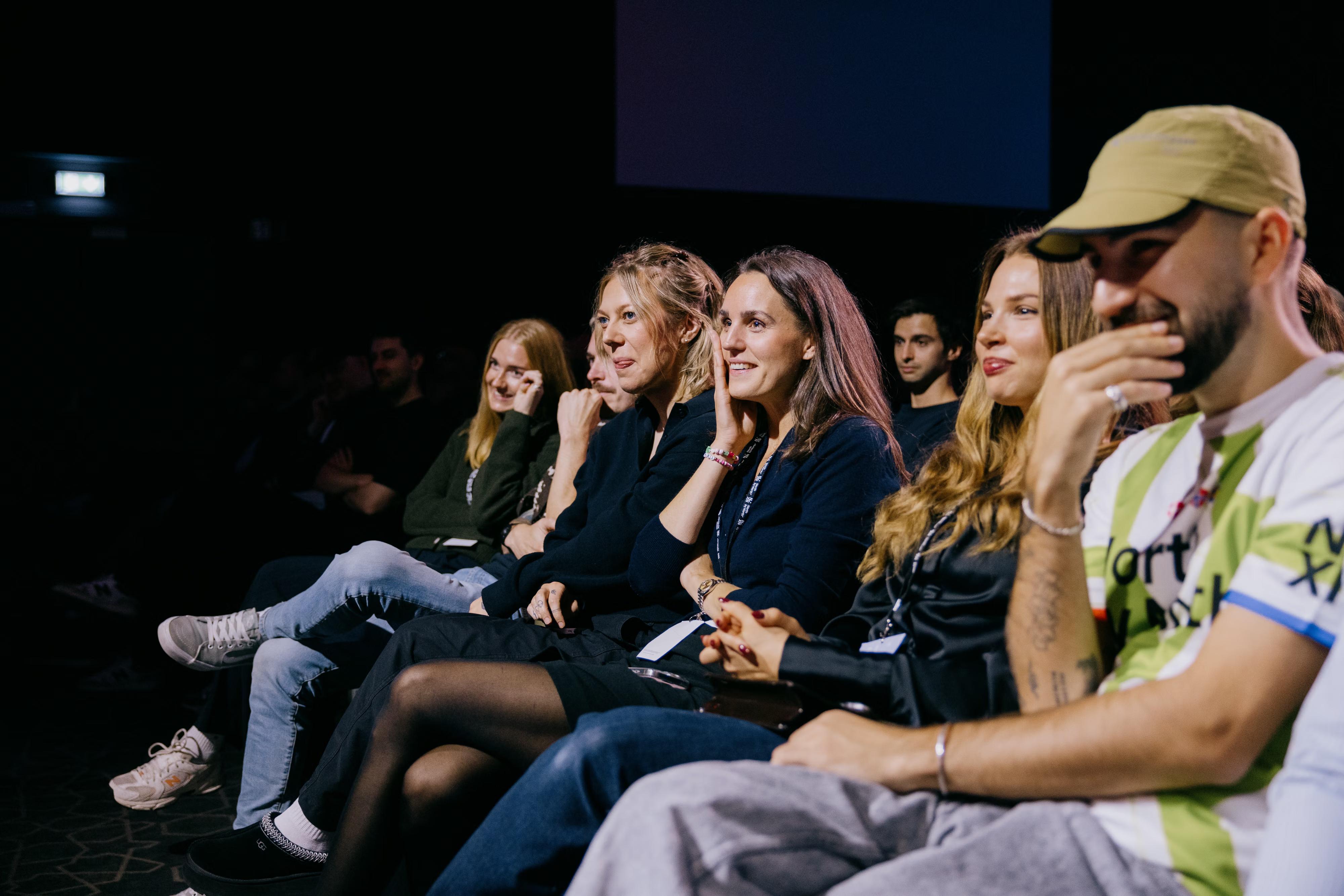 Audience members smiling and engaged in a dark room.