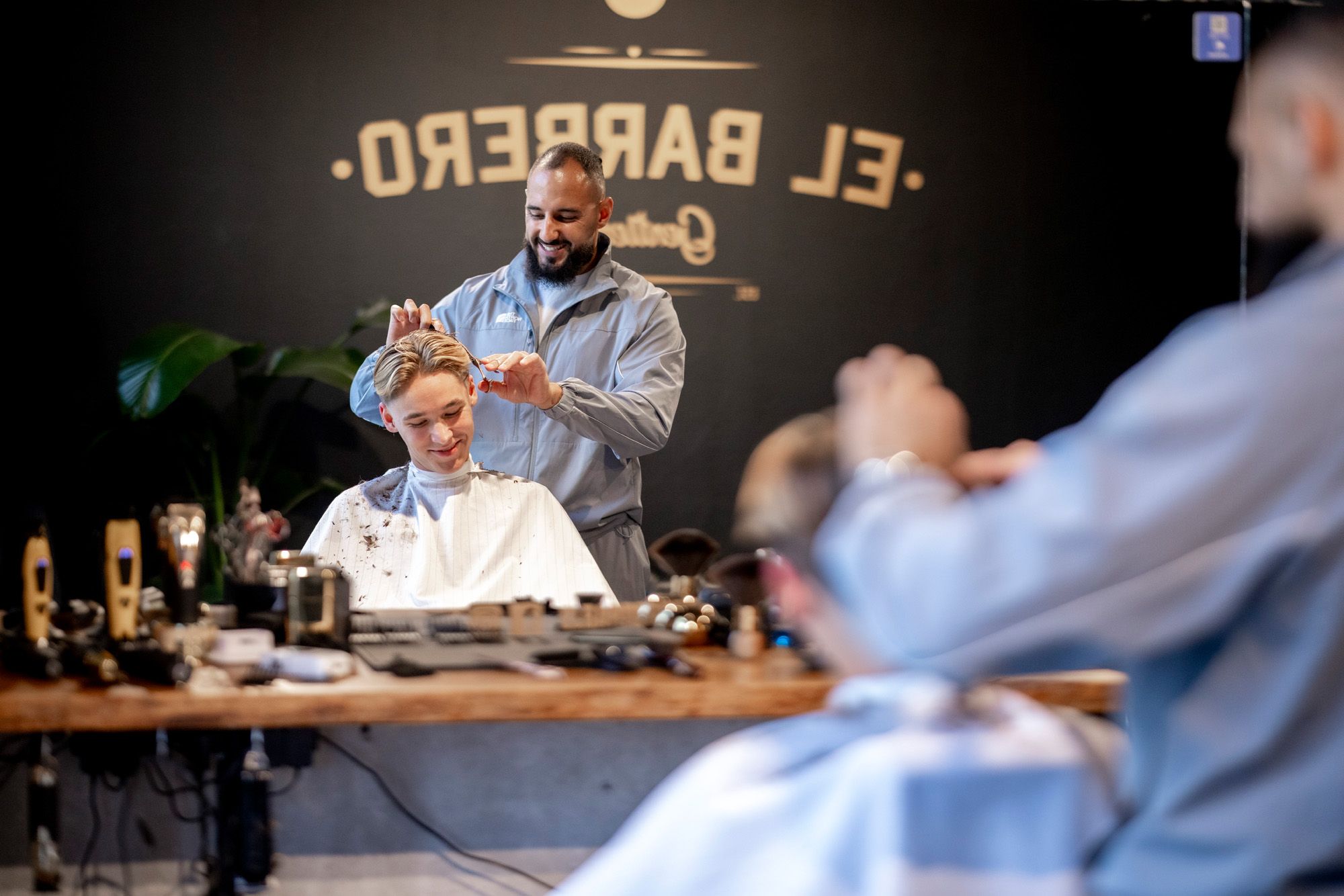 A barber gives a smiling young man a haircut in a barbershop.