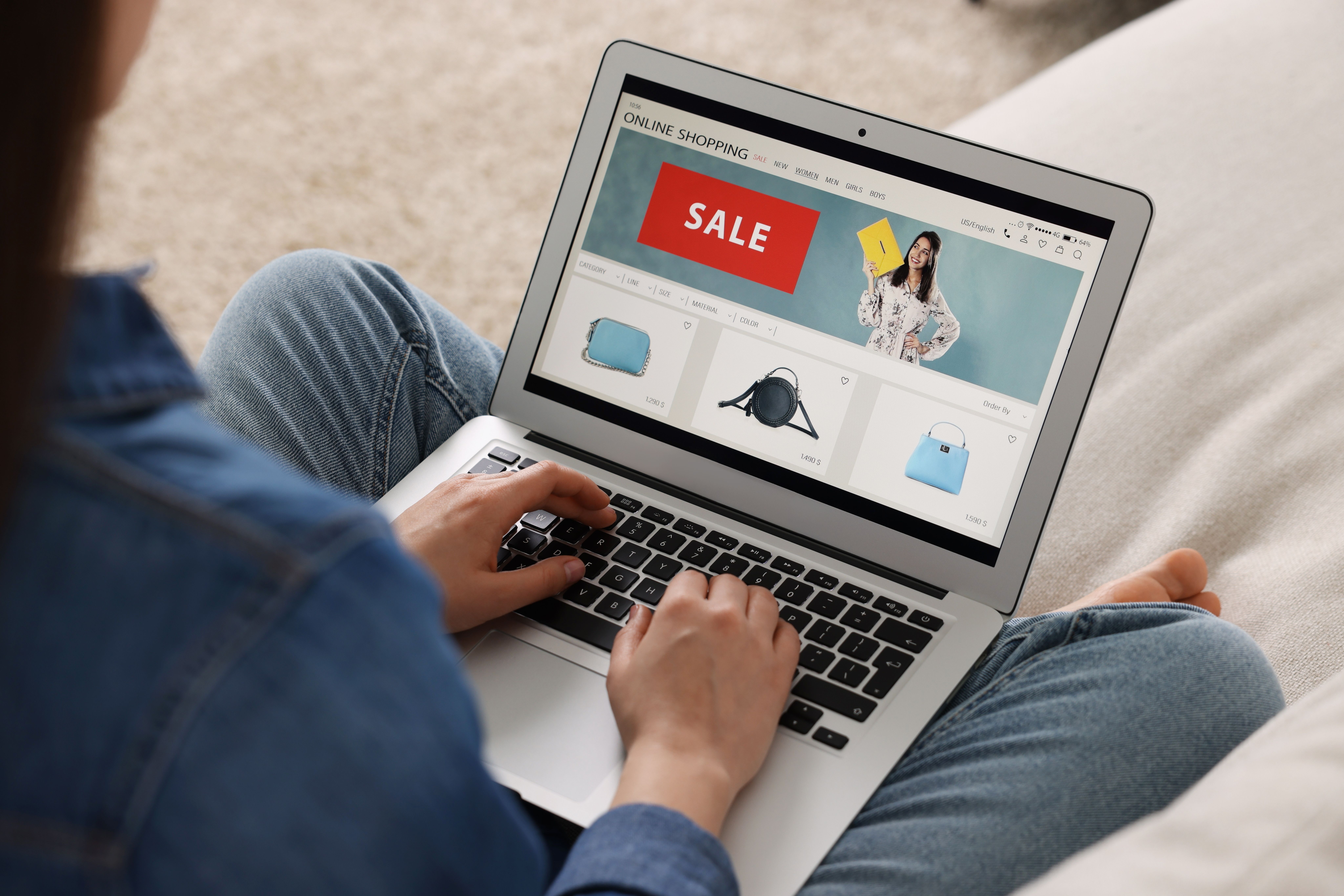 A person shops for handbags online on a laptop, with a prominent 'SALE' banner displayed.